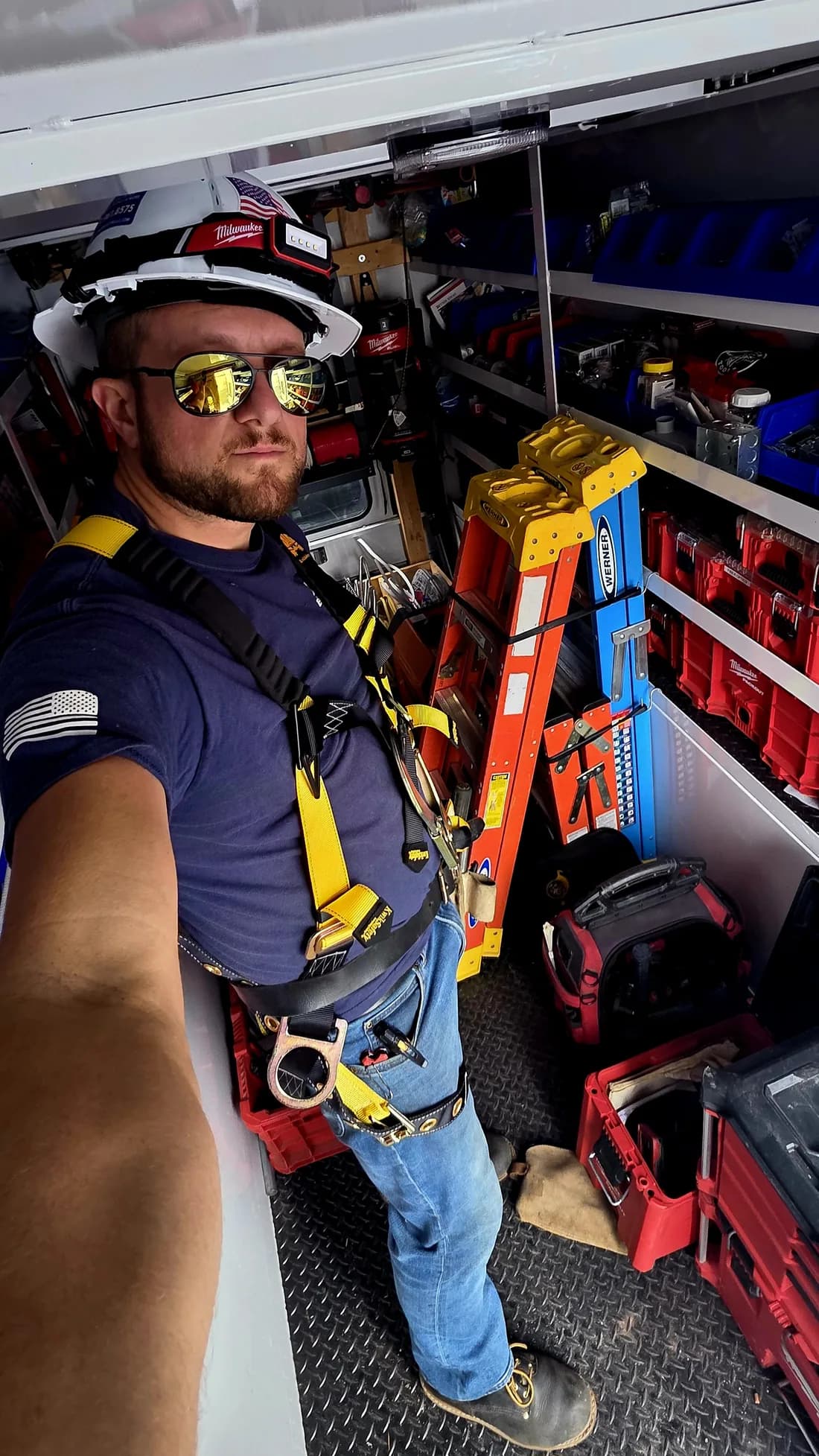 Slon Electric electrician in a hard hat and fall arrest harness in a stocked work van