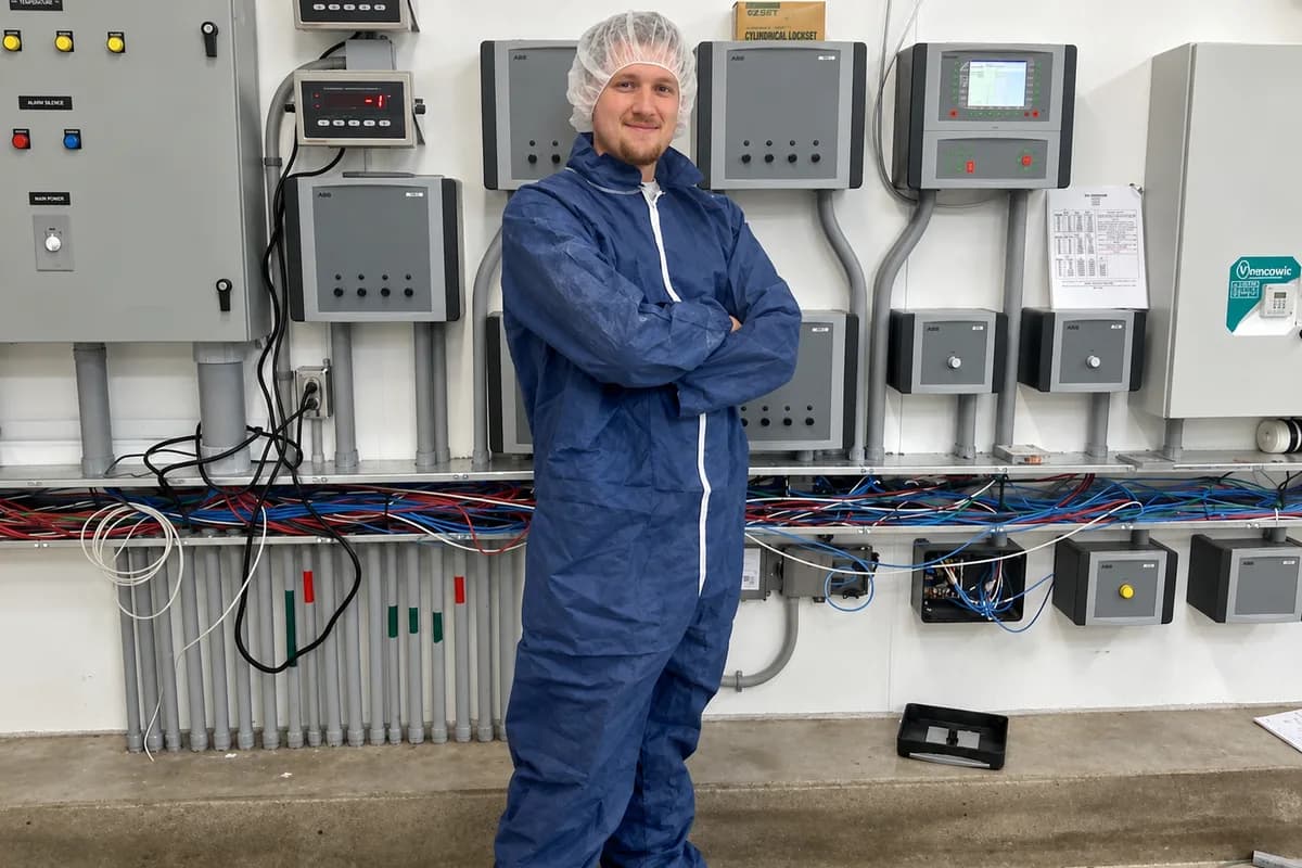 Electrician in protective coveralls standing in front of a bank of control panels