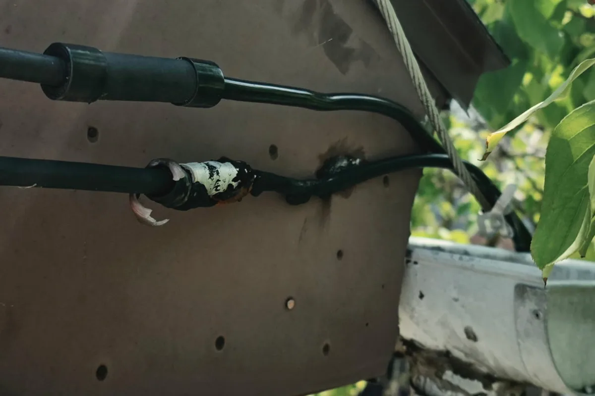 Burned and damaged service drop splice at a building, scorch marks visible on the wire and wall